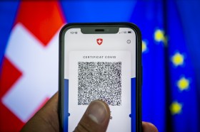 Il certificato covid su un telefonino con sullo sfondo le bandiere della Svizzera e dell Ue.