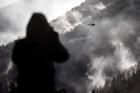 Un uomo osserva da lontano un elicottero che getta acqua sull incendio.