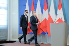 due uomini in giacca e cravatta con mascherine camminano davanti a bandiere svizzere e polacche