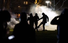 manifestanti controluce, di notte, uno sta prendendo a calcio qualcosa