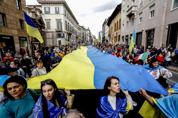 corteo di persone sfila con una grande bandiera ucraina