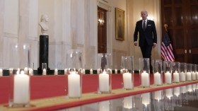 Joe Biden cammina in un corridoio della Casa Bianca con candele a lato.