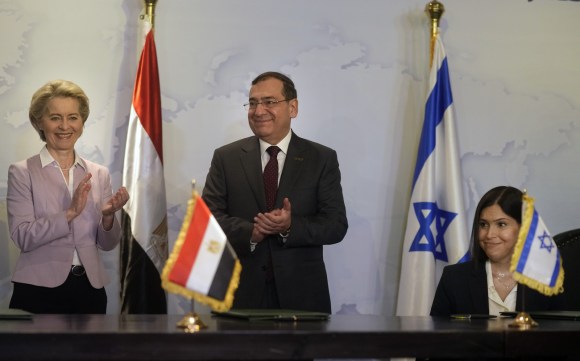 un uomo e una donna in piedi sorridono, un altra donna è seduta. davanti e dietro a loro le bandiere egiziana e israeliana