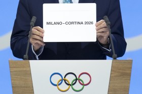 uomo mostra cartello con scritta Milano-Cortina 2026