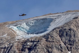 elicottero vola sopra un ghiacciaio sul quale è visibile il buco lasciato dal distacco del seracco