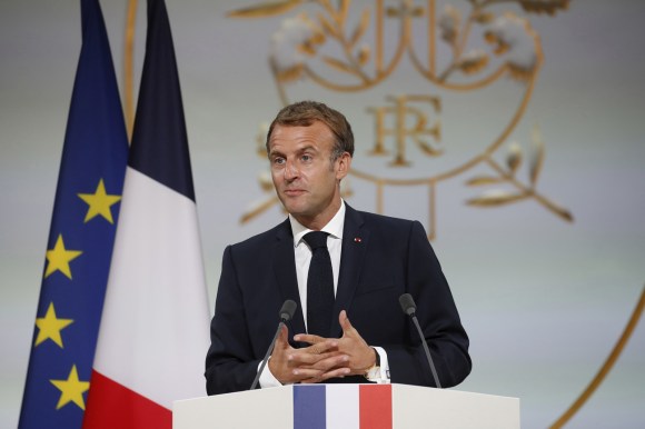 uomo in giacca a cravatta parla dietro a un pulpito. dietro di lui la bandiera francese e quella dell UE