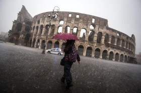 Una donna con un ombrello rosso davanti al Colosseo in un giorno di pioggia torrenziale.