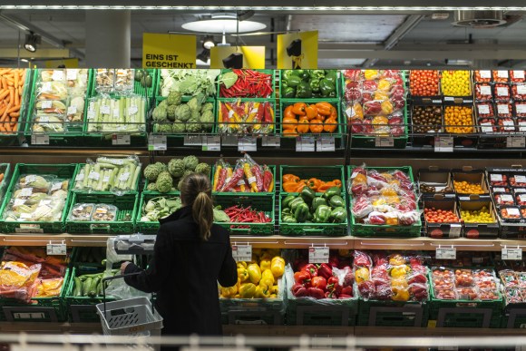 Una giovane donna di spalle davanti al bancone delle verdure in un supermercato.