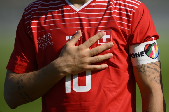 busto di uomo con maglia nazionale svizzera di calcio e fascia sul bicipite sinistro con cuore con colori arcobaleno