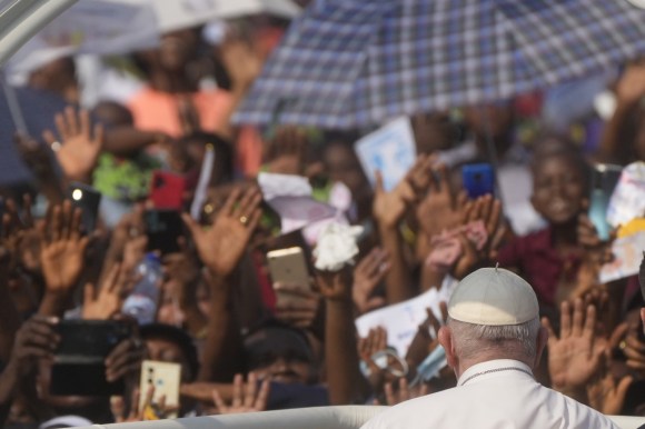 papa fotografato di spalle di fronte a folla di fedeli africani