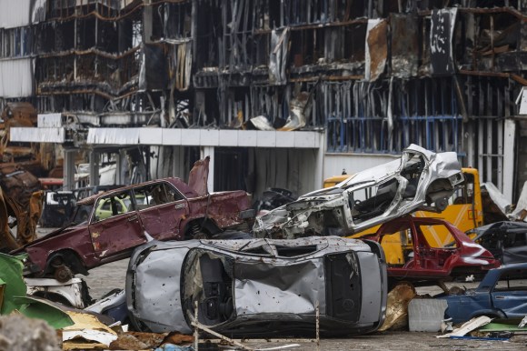 carcasse di veicoli impilate davanti a edificio distrutto