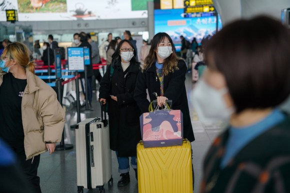 viaggiatori cinesi in aeroporto con lmascherine e valigie