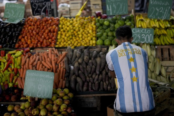 uomo seduto davanti a cassette di frutta e verdura, fotografato di spalle, indossa la maglia della nazionale argentina
