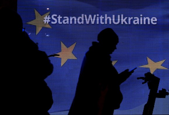 sagoma di persona in scuro che guarda il telefonino su bandiera ue con scritta #standwithukraine