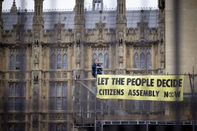 Aktivist ist mit Aufruf für Bürgerpanels auf einem Zaun vor dem Westminster Palast