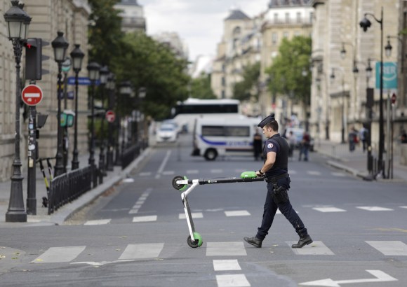 poliziotto attraversa una strada con un monopattino elettrico tra le mani