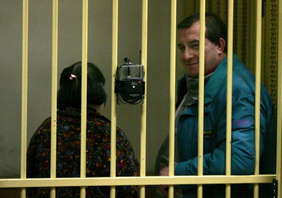 due perosne dietro le sbarre: una donna voltata di spalle e un uomo che guarda in camera sorridendo