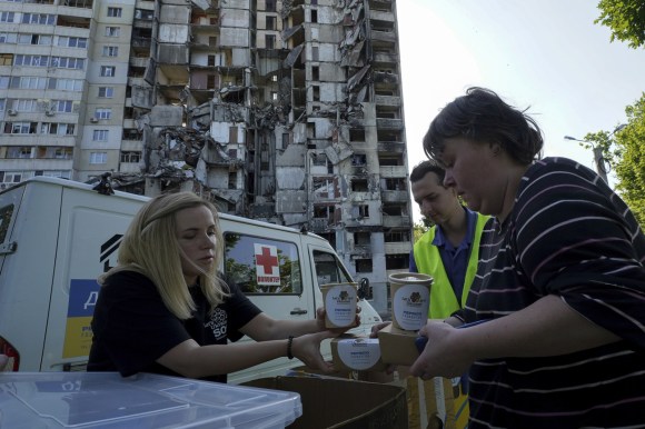 persona distribuisce cibo ad altre persone davanti a un edificio distrutto