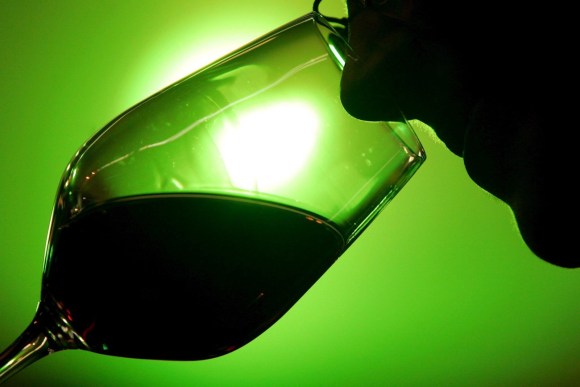 primissimo piano di uomo che annusa bicchiere di vino rosso in controluce di una lampadina verde