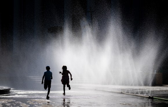 Due bambini giocano con degli spruzzi d acqua in piazza federale a Berna.