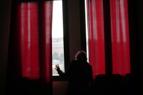 Una donna si affaccia alla finestra coperta da tende rosse