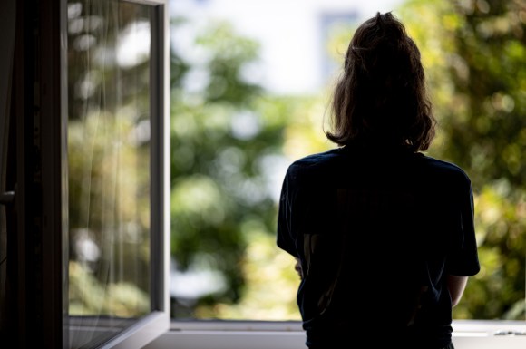 Una donna fotografata di spalle che guarda da una finestra.