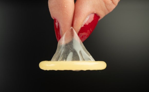 primo piano su un preservativo arrotolato tenuto tra il pollice e l indice di una donna con le unghie dipinte di rosso