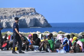 migranti seduti per terra in un porto