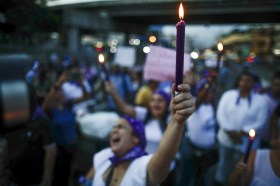 una donna tiene in mano una candela ross accesa nel corso di una protesta