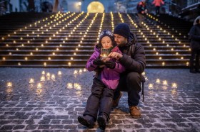 Un uomo con una bambina seduta sulle gambe e dietro le luci delle candele accese.